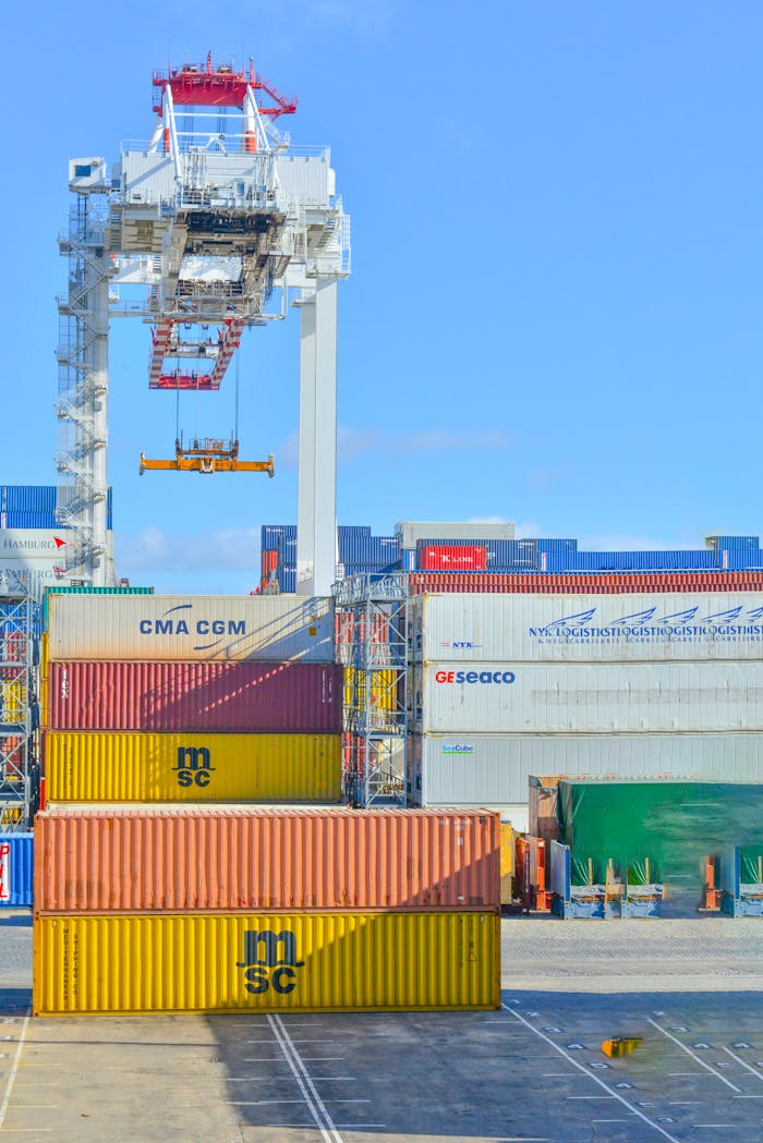 hero-img-01 Stacked cargo containers in a sunny port industrial setting with crane.